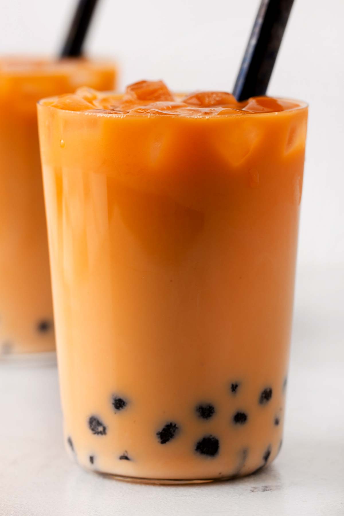 Thai bubble tea in a clear glass with ice and an extra wide straw.