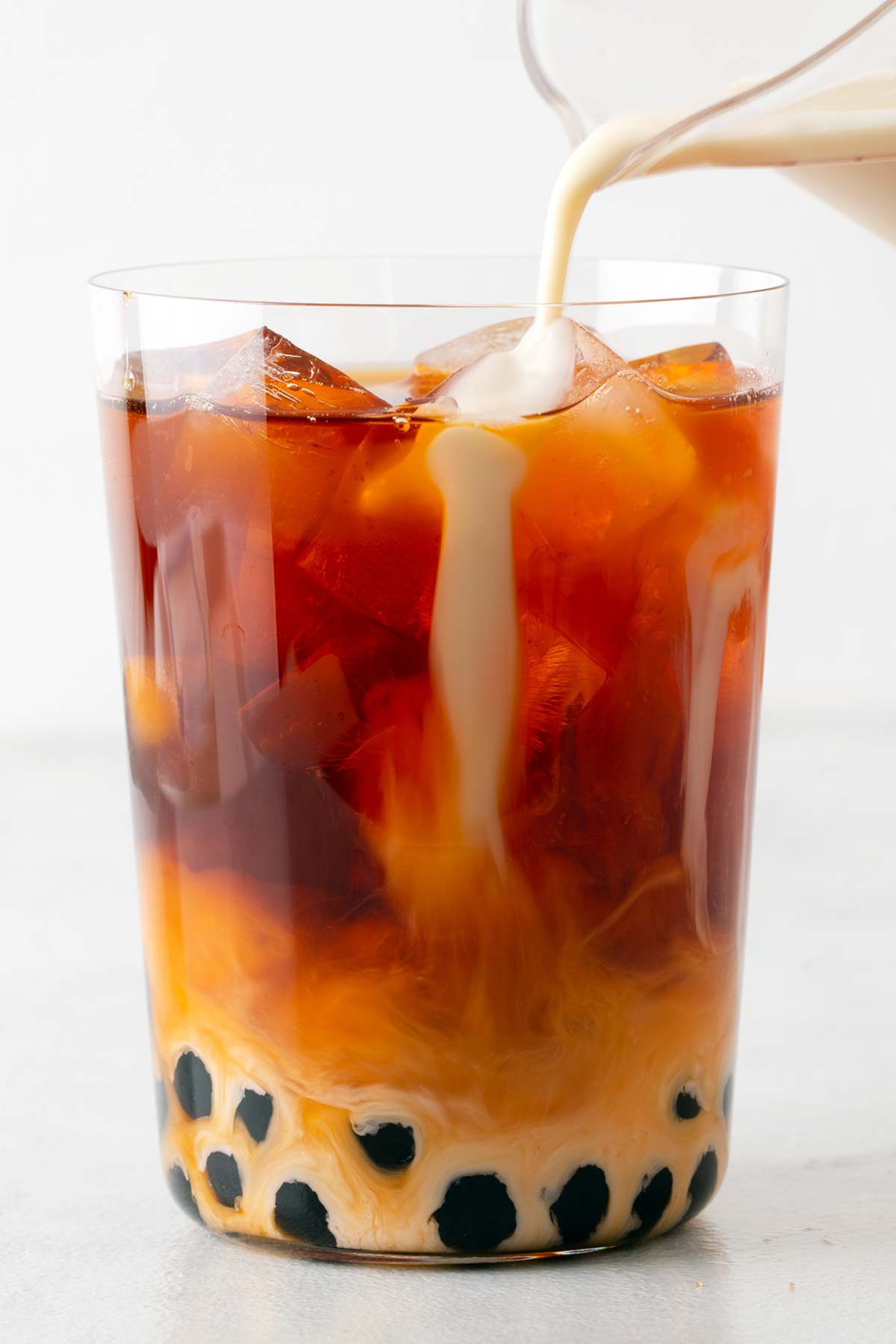 Pouring sweetened condensed milk and evaporated milk into a cup of Thai iced tea with boba.